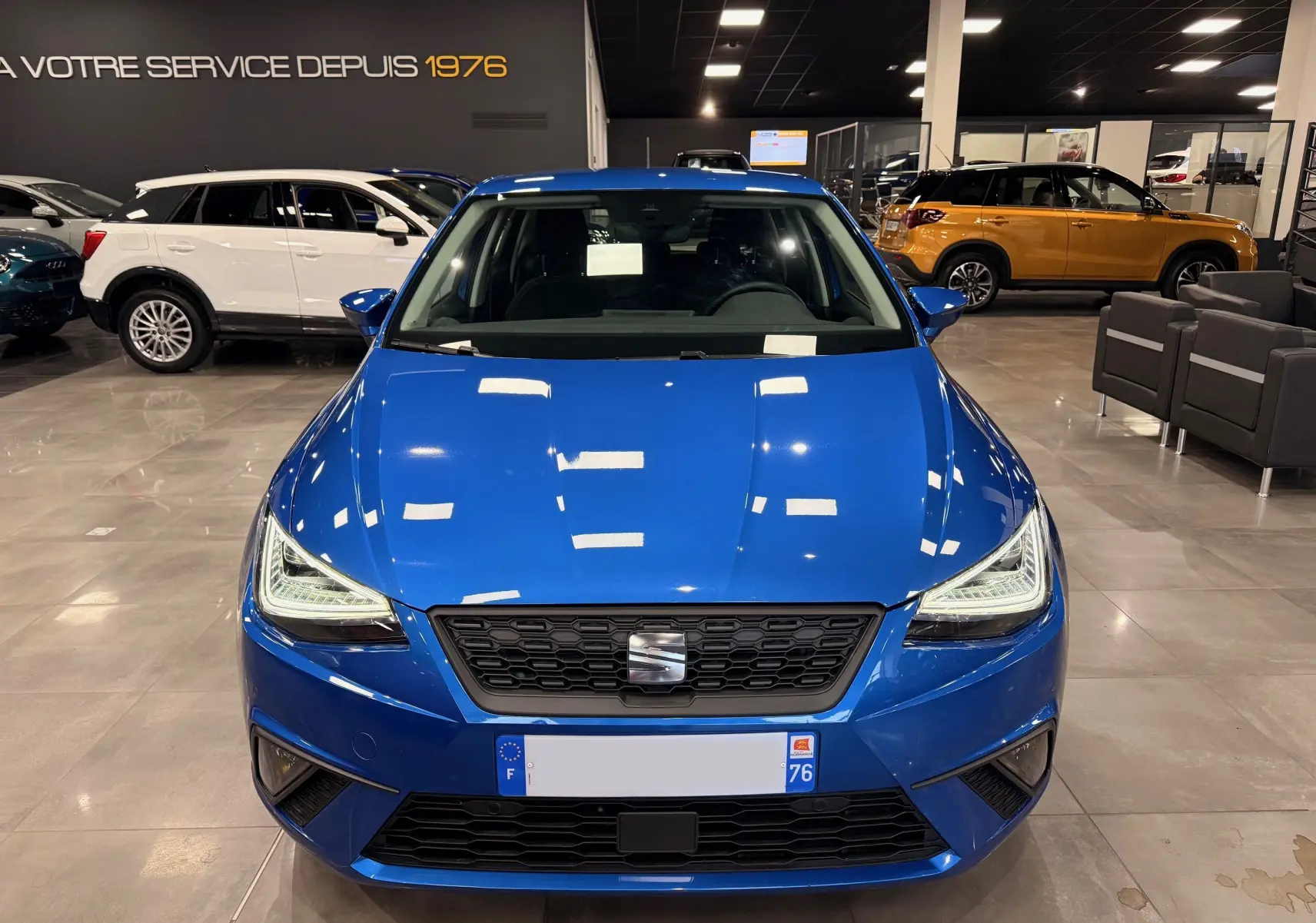 Vue avant d'une SEAT Ibiza 1.0 TSI 95CH Copa bleu vif dans un showroom, avec phares LED et calandre noire.