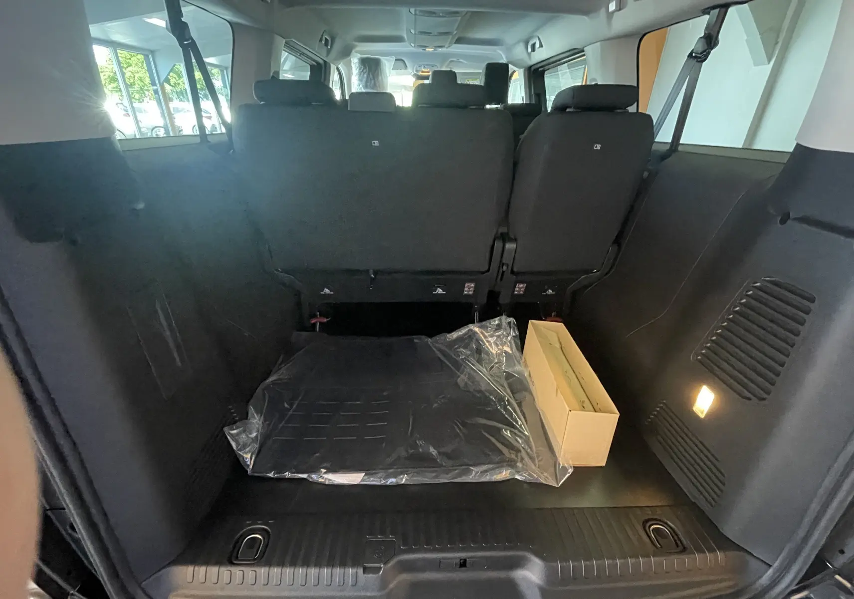 Intérieur coffre arrière du Peugeot Traveller noir 2026, montrant les sièges rabattus et un carton posé au sol.