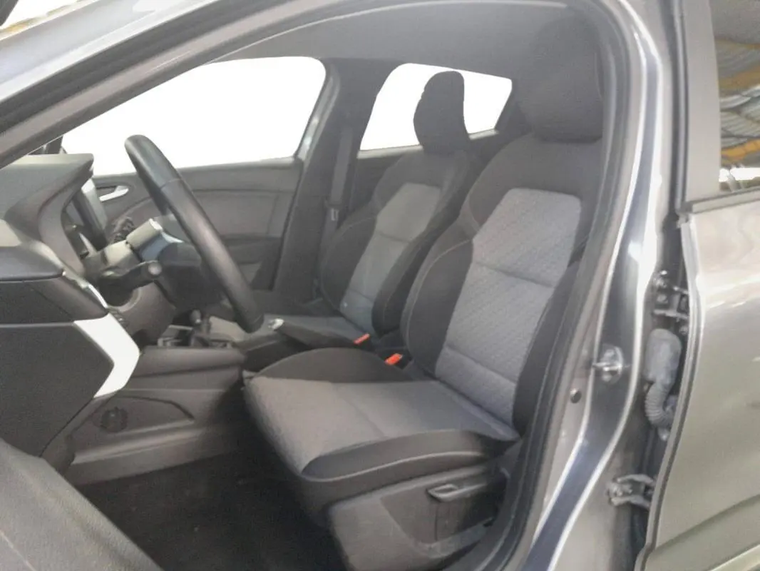 Vue intérieure côté conducteur de la Renault Clio gris clair 2023, sièges tissu bi-tons et tableau de bord moderne.