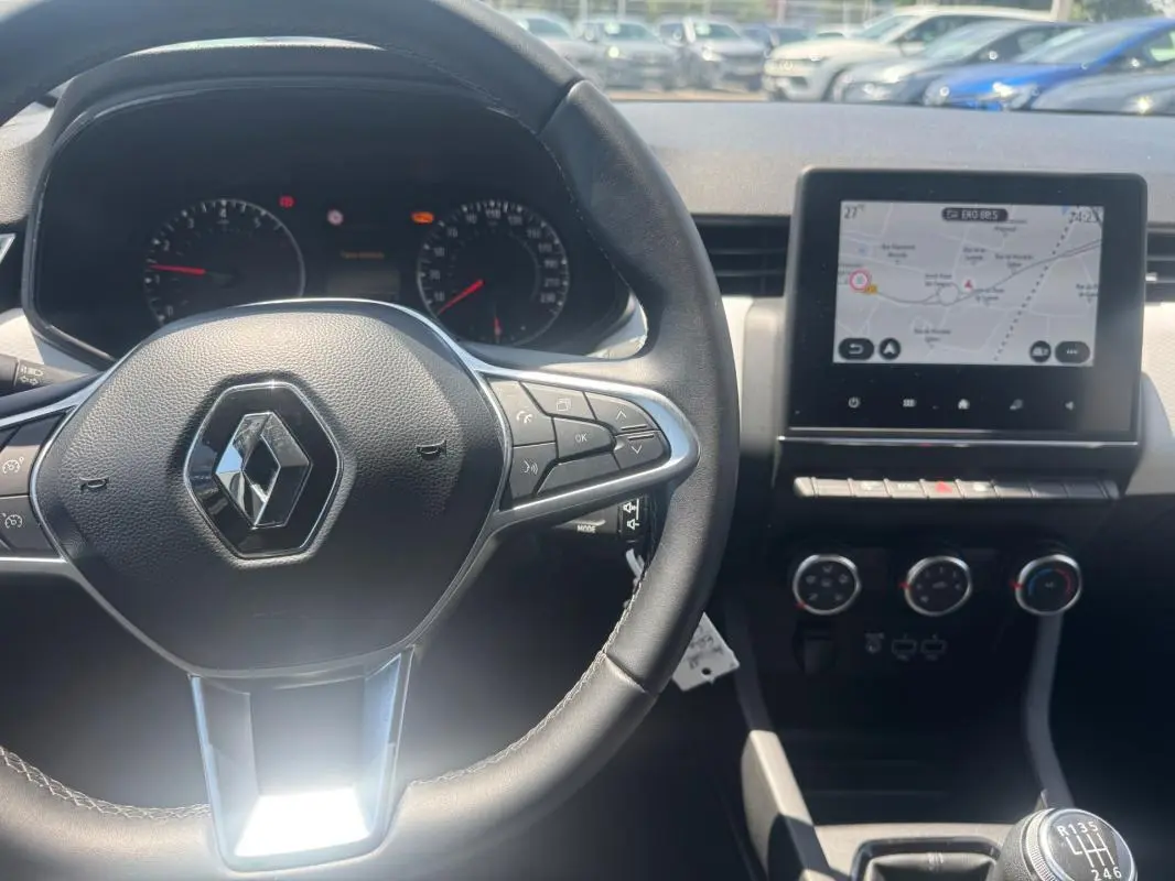Intérieur Renault Clio 2023 vu du poste de conduite, volant multifonction et écran tactile avec navigation visible.