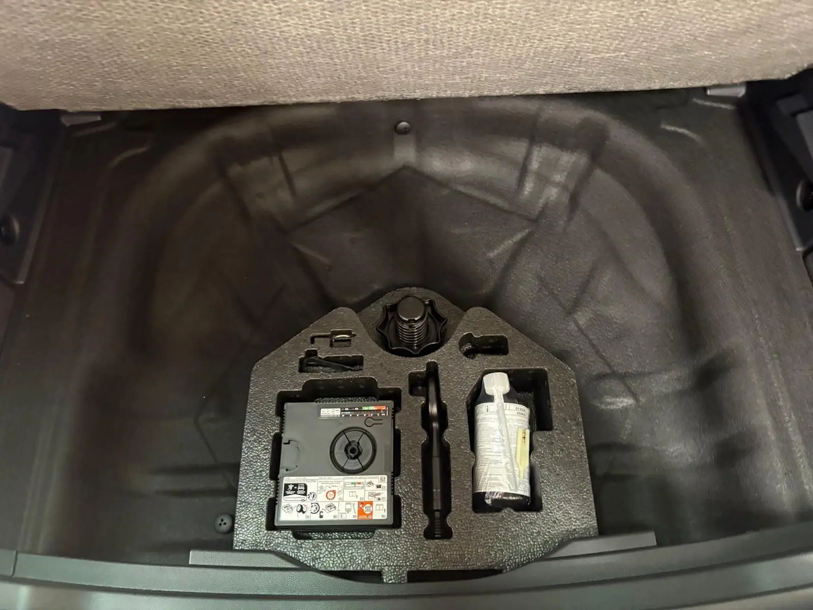 Coffre ouvert d'un SEAT Ateca 2.0 TDI 150 DSG7 Copa 2025 gris graphite, montrant le kit de réparation pneus rangé.