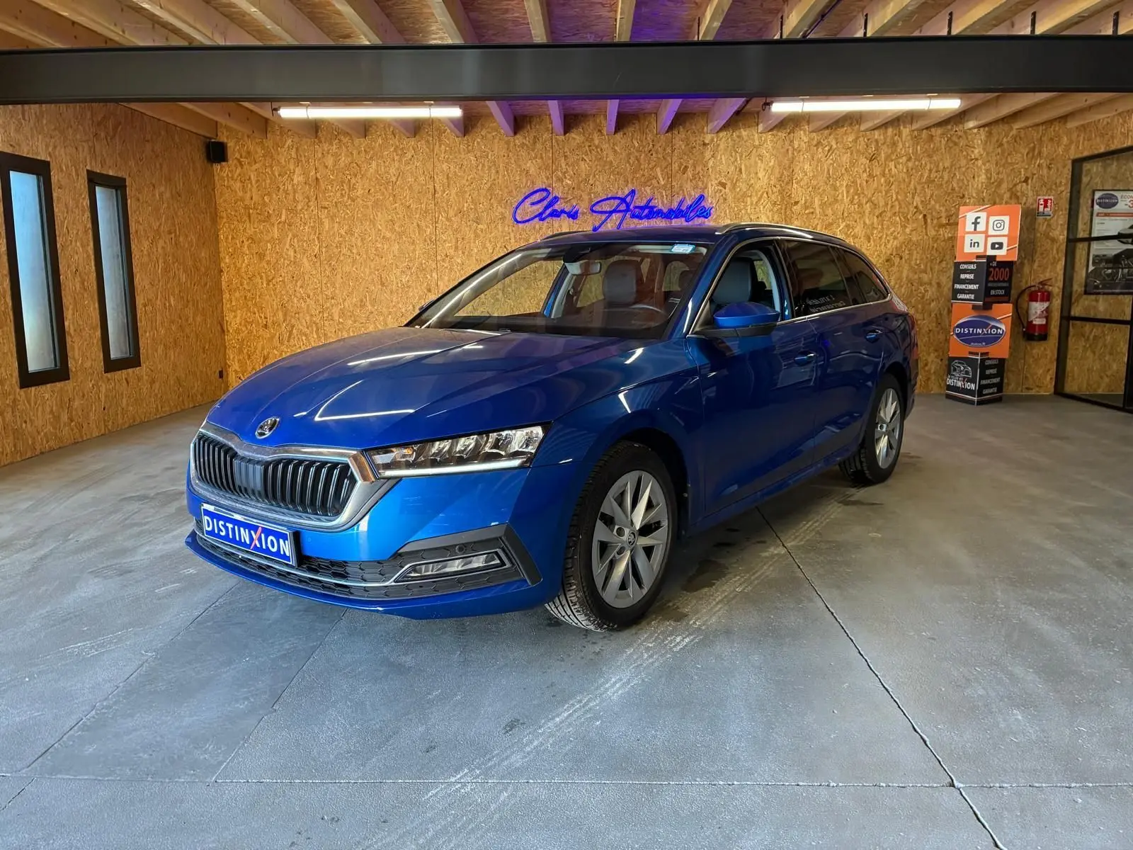 SKODA OCTAVIA COMBI 2024 bleu en 3/4 avant droit, avec calandre chromée et phares LED dans un showroom.