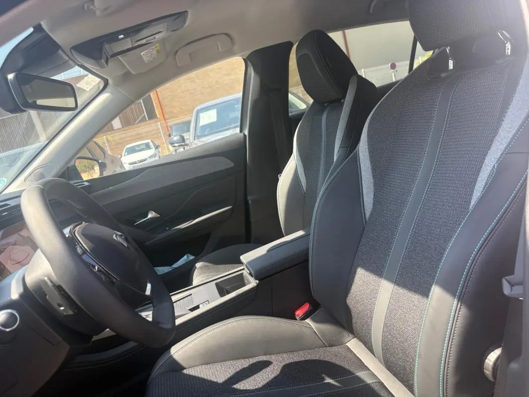 Vue intérieure côté conducteur du Peugeot 308 PHEV 180 e-EAT8 Allure 2024, sièges tissu et cuir gris, volant multifonction.