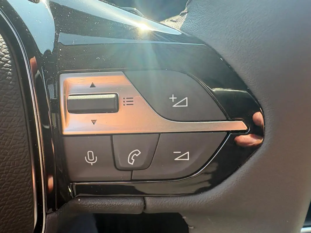 Gros plan sur les commandes multifonctions du volant de la Peugeot 308 PHEV 180 e-EAT8 Allure 2024 gris clair.