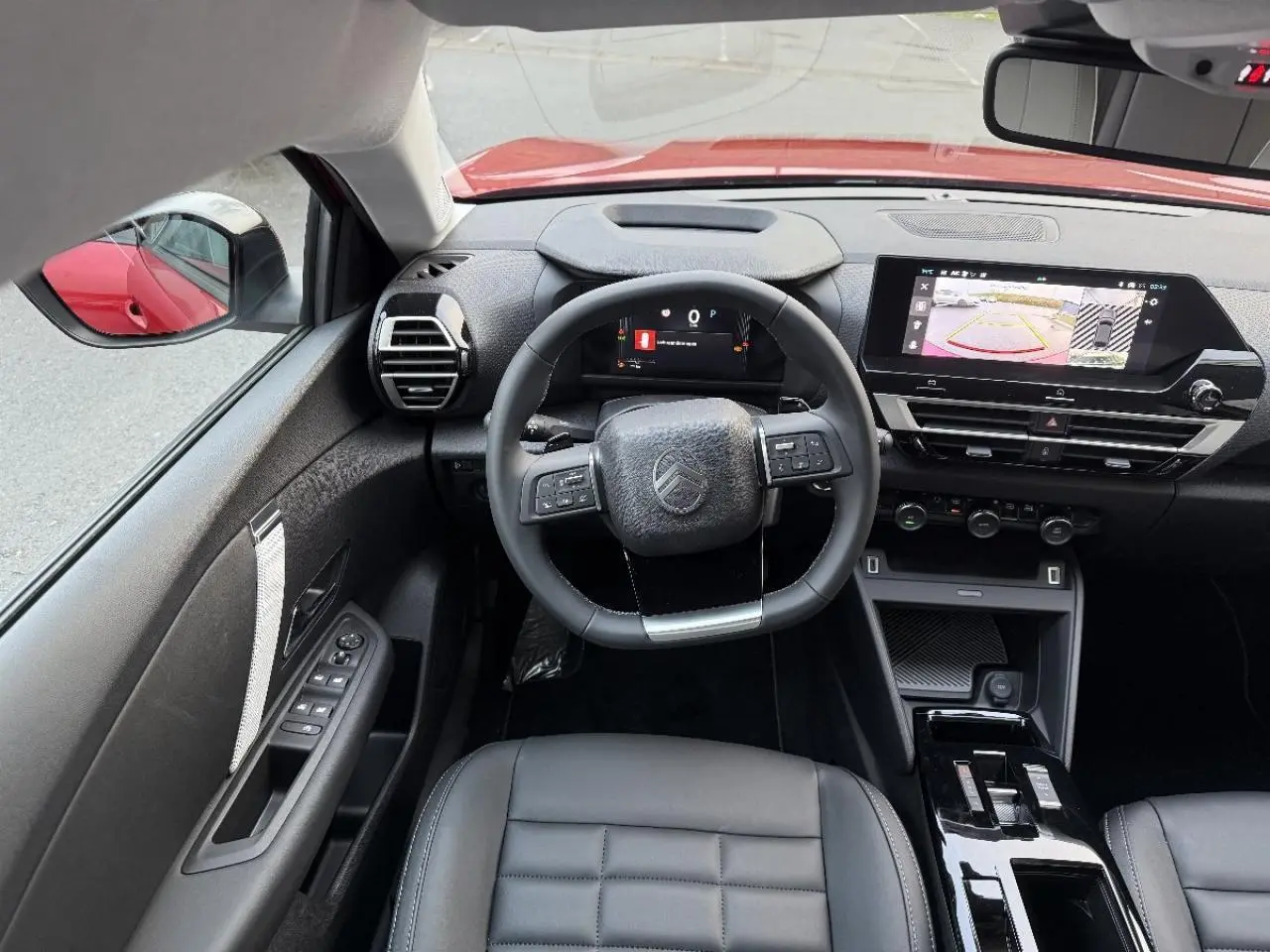 Intérieur de la Citroën C4 2025 rouge elexir, vue du poste de conduite avec volant multifonction et écran tactile central.