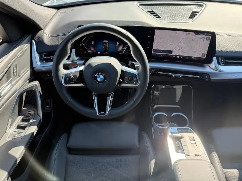 Vue intérieure centrée sur le volant cuir noir et l'écran tactile large du tableau de bord de la BMW X2 2025.