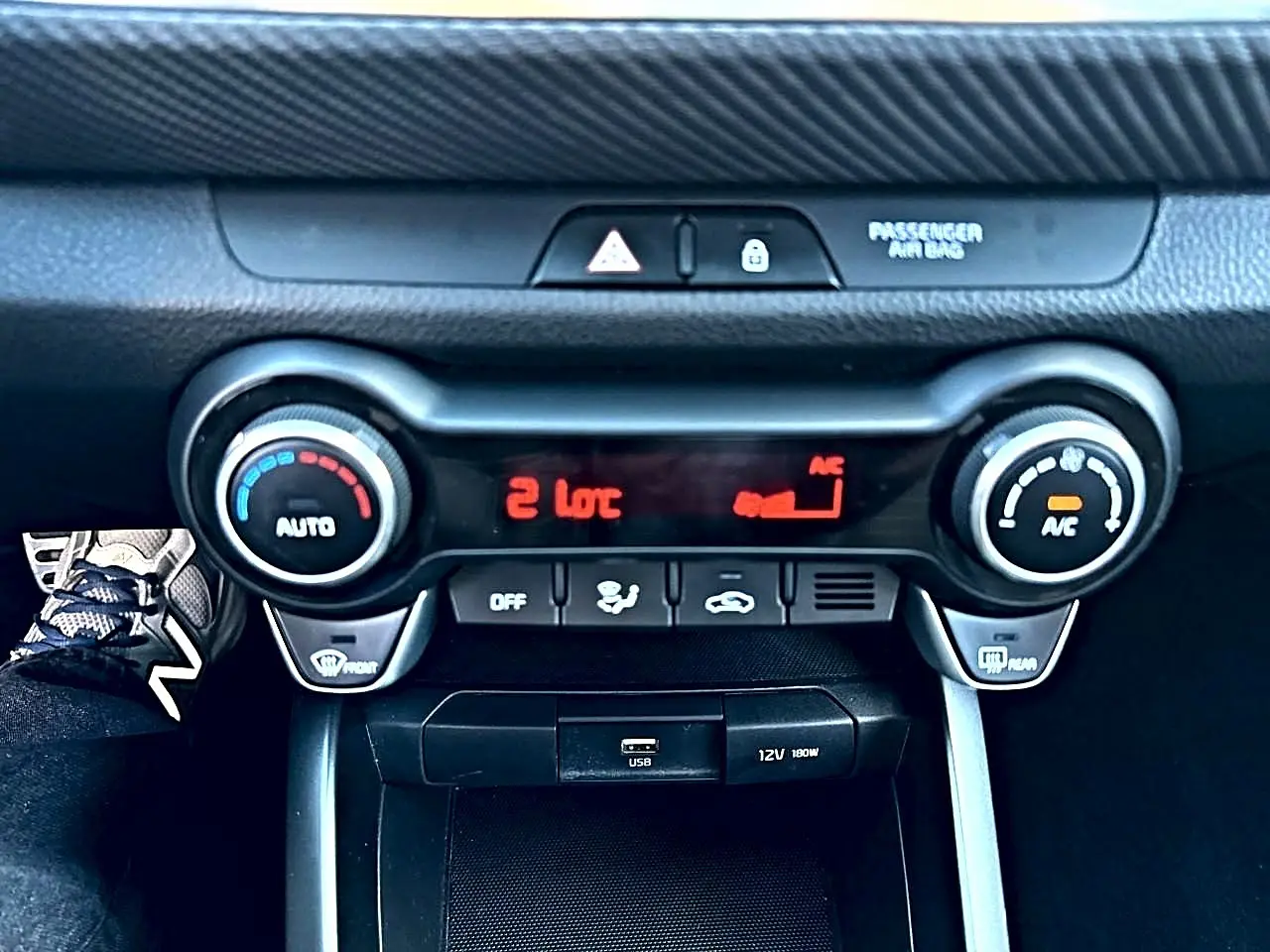 Vue rapprochée de la console centrale noire du Kia Stonic 2025, avec commandes de climatisation et ports USB/12V visibles.