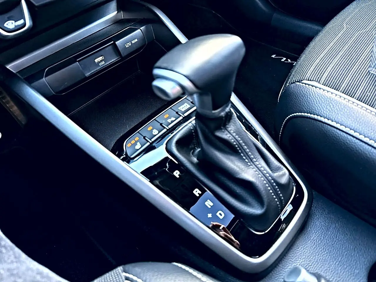 Gros plan sur le levier de vitesses automatique noir et cuir, entouré de commandes et console grise du Kia Stonic gris.