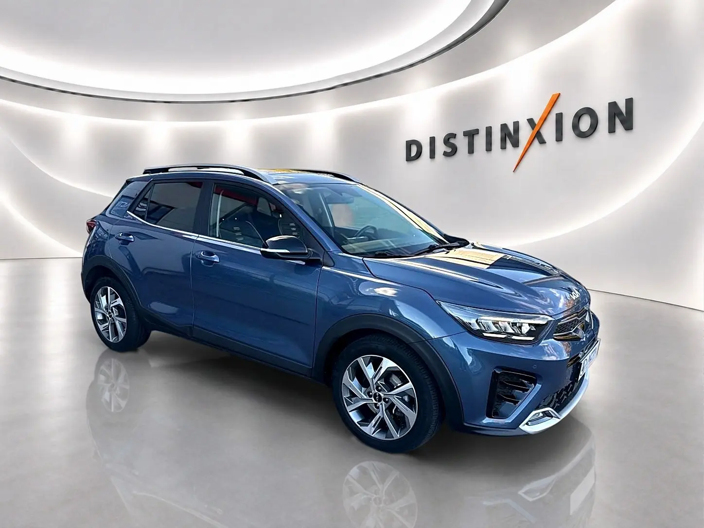 KIA Stonic gris en vue 3/4 avant droit, avec jantes alliage et barres de toit visibles dans un showroom lumineux.