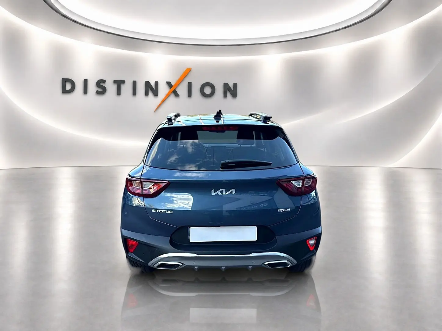 Vue arrière d'un KIA Stonic gris avec double sortie d'échappement et barres de toit dans un showroom lumineux.