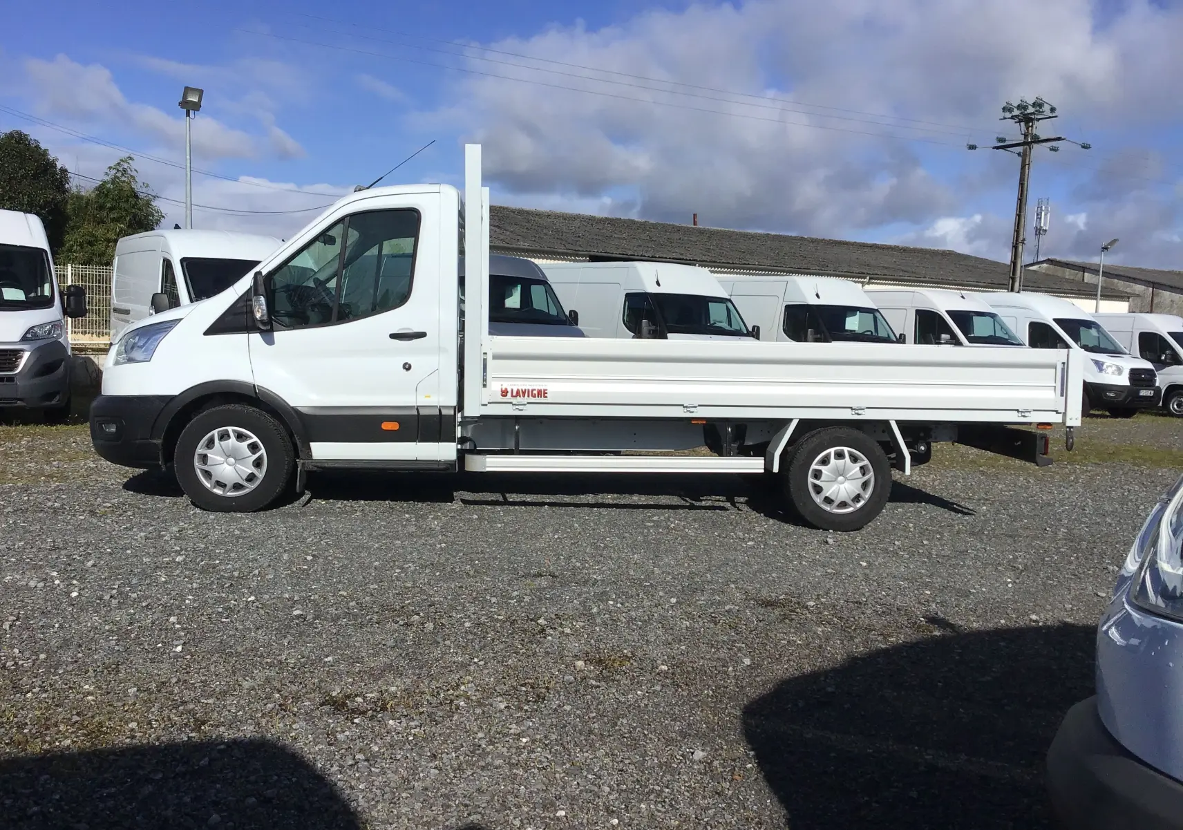 Ford Transit Chassis Cabine blanc vu de profil côté gauche avec plateau 4 mètres et ridelles en aluminium.