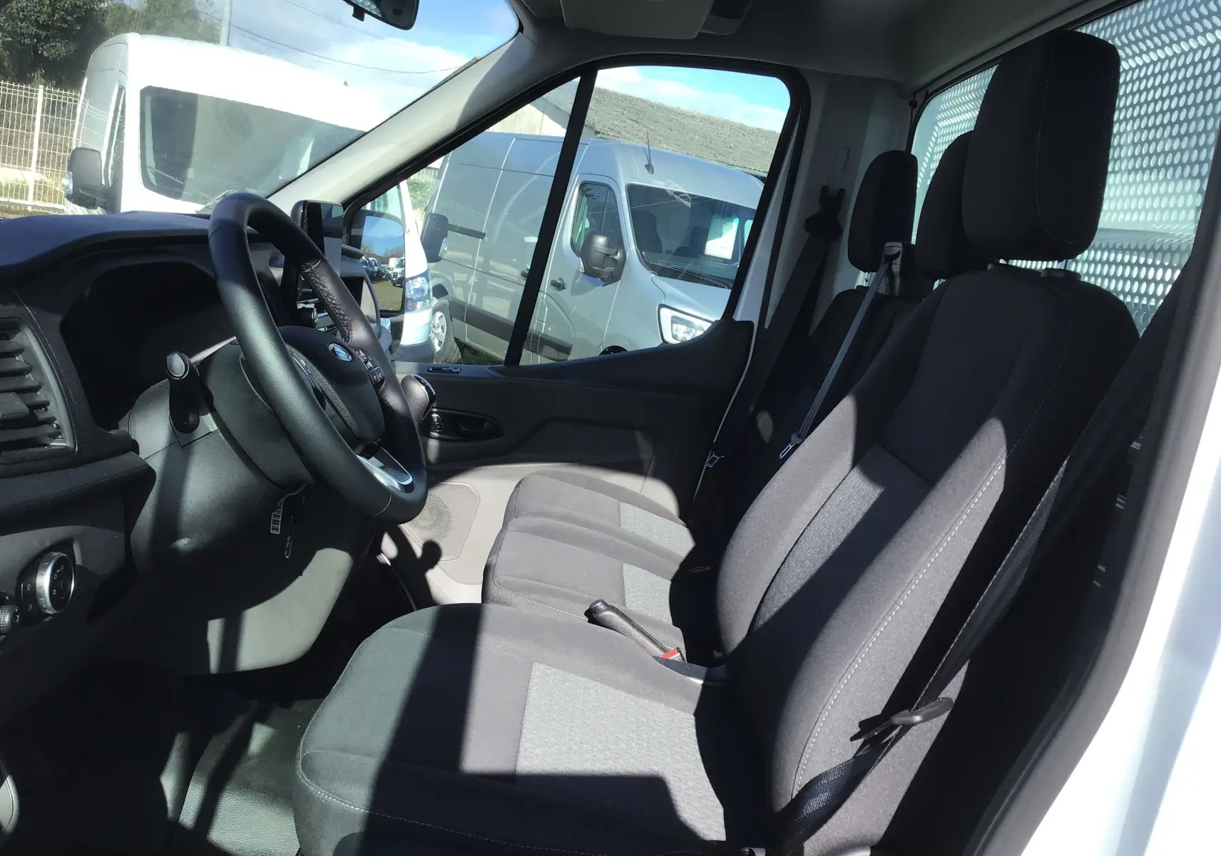 Vue intérieure côté conducteur du Ford Transit Chassis Cabine blanc, montrant les sièges avant et le volant.