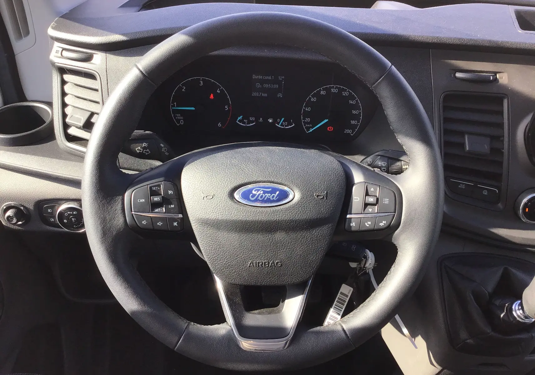 Vue rapprochée du volant noir du Ford Transit Chassis Cabine 2020 avec tableau de bord et levier de vitesses manuel visible.