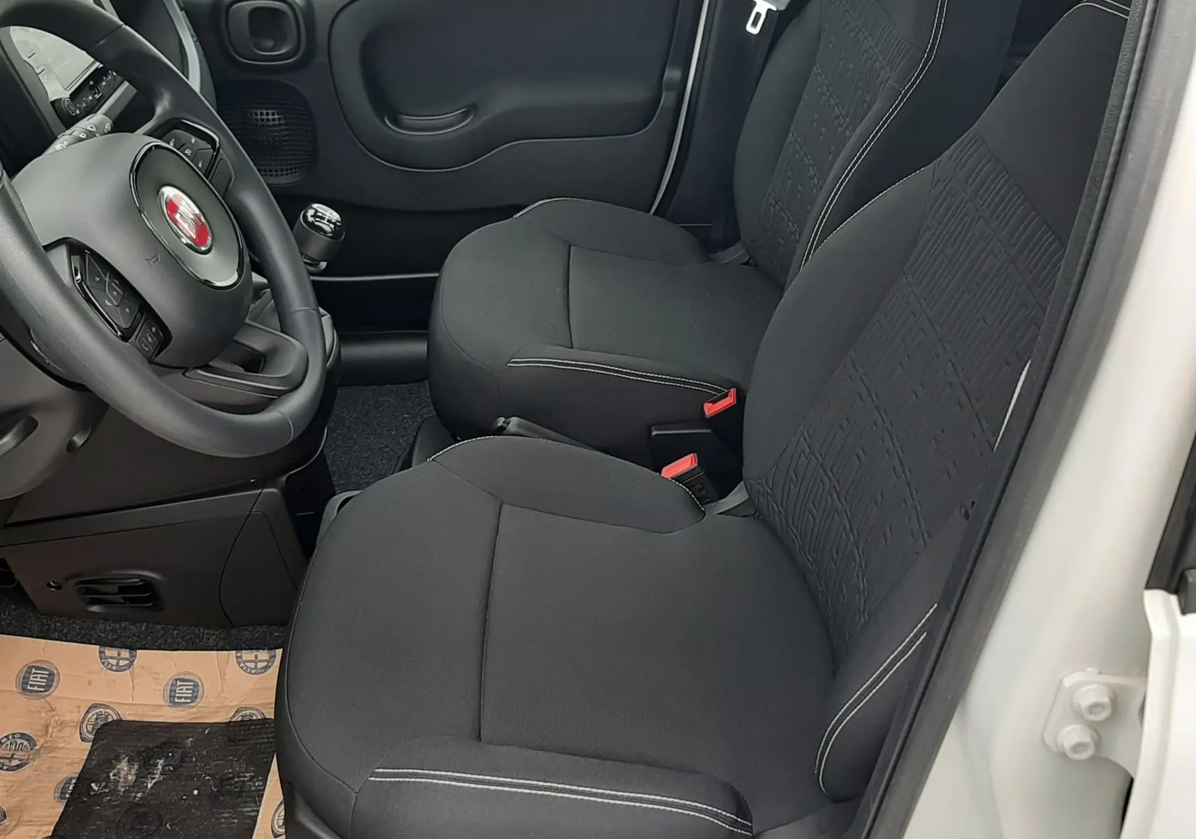 Vue intérieure côté conducteur de la Fiat Panda blanc gelato 2025, sièges tissu noir avec volant multifonction.
