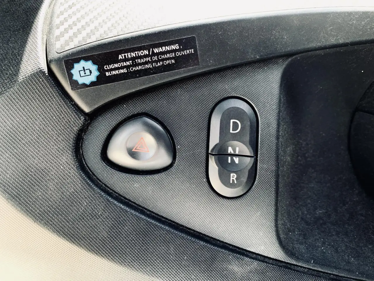 Gros plan sur la commande de boîte automatique et le bouton de warning dans l'habitacle noir d'une Renault Twizy blanche.