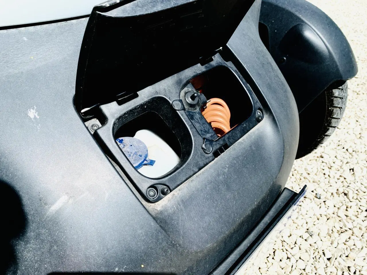 Gros plan sur la trappe de charge ouverte de la Renault Twizy blanche, montrant le câble spiralé orange et le bouchon de réservoir.