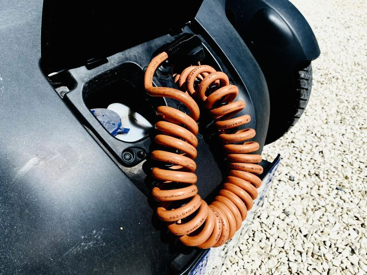 Gros plan sur le câble de charge orange enroulé dans la trappe de recharge d’une Renault Twizy blanche, vue arrière droite.