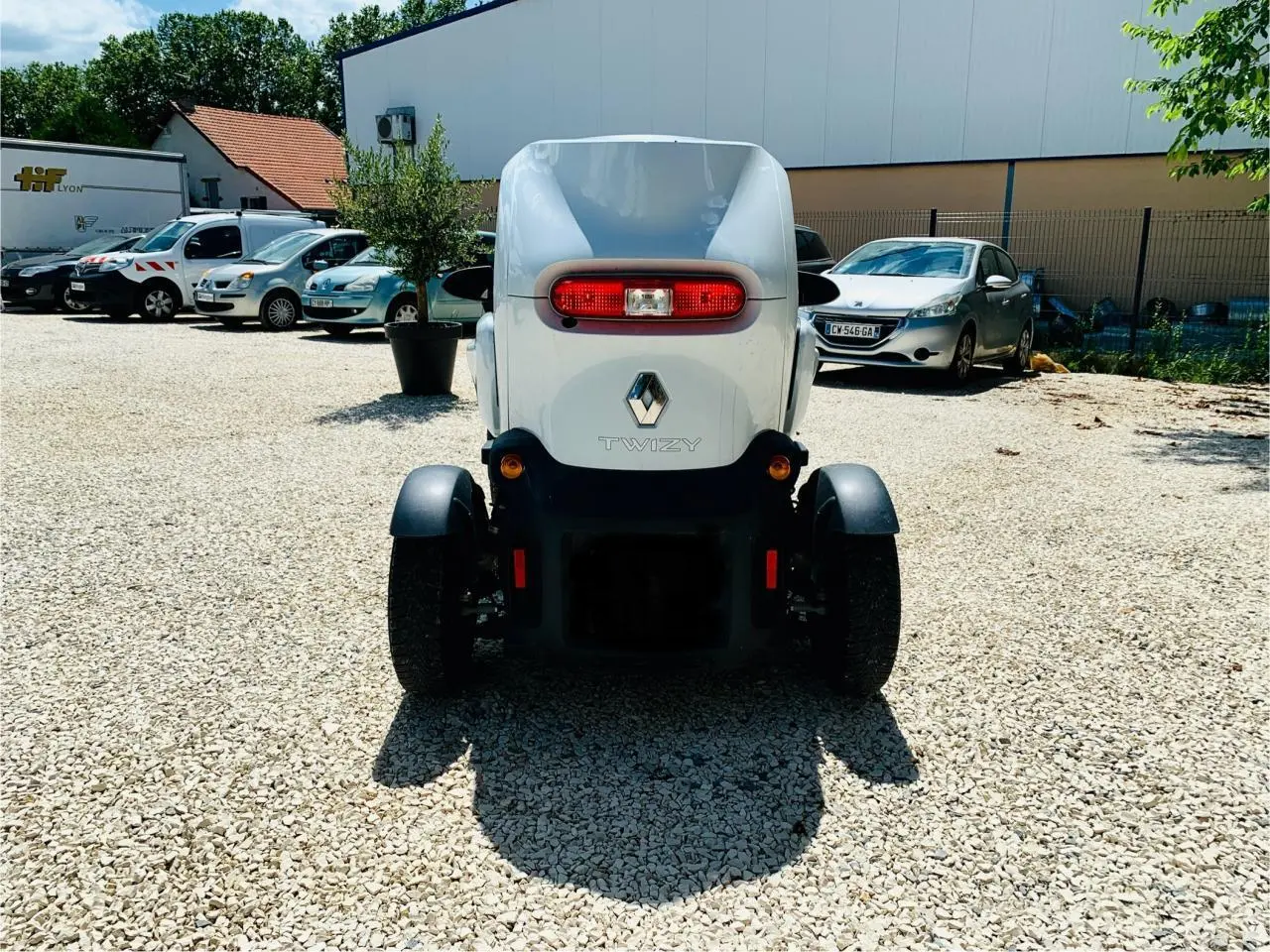 Vue arrière d'une Renault Twizy blanche électrique, avec feu arrière ovale rouge et logo Renault visible.