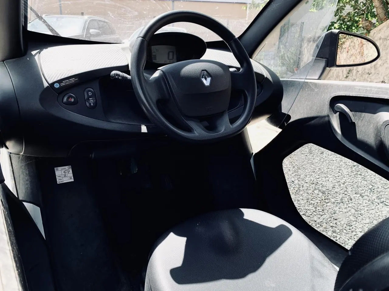 Vue intérieure côté conducteur du tableau de bord et volant noir avec logo Renault d'une Renault Twizy blanche.