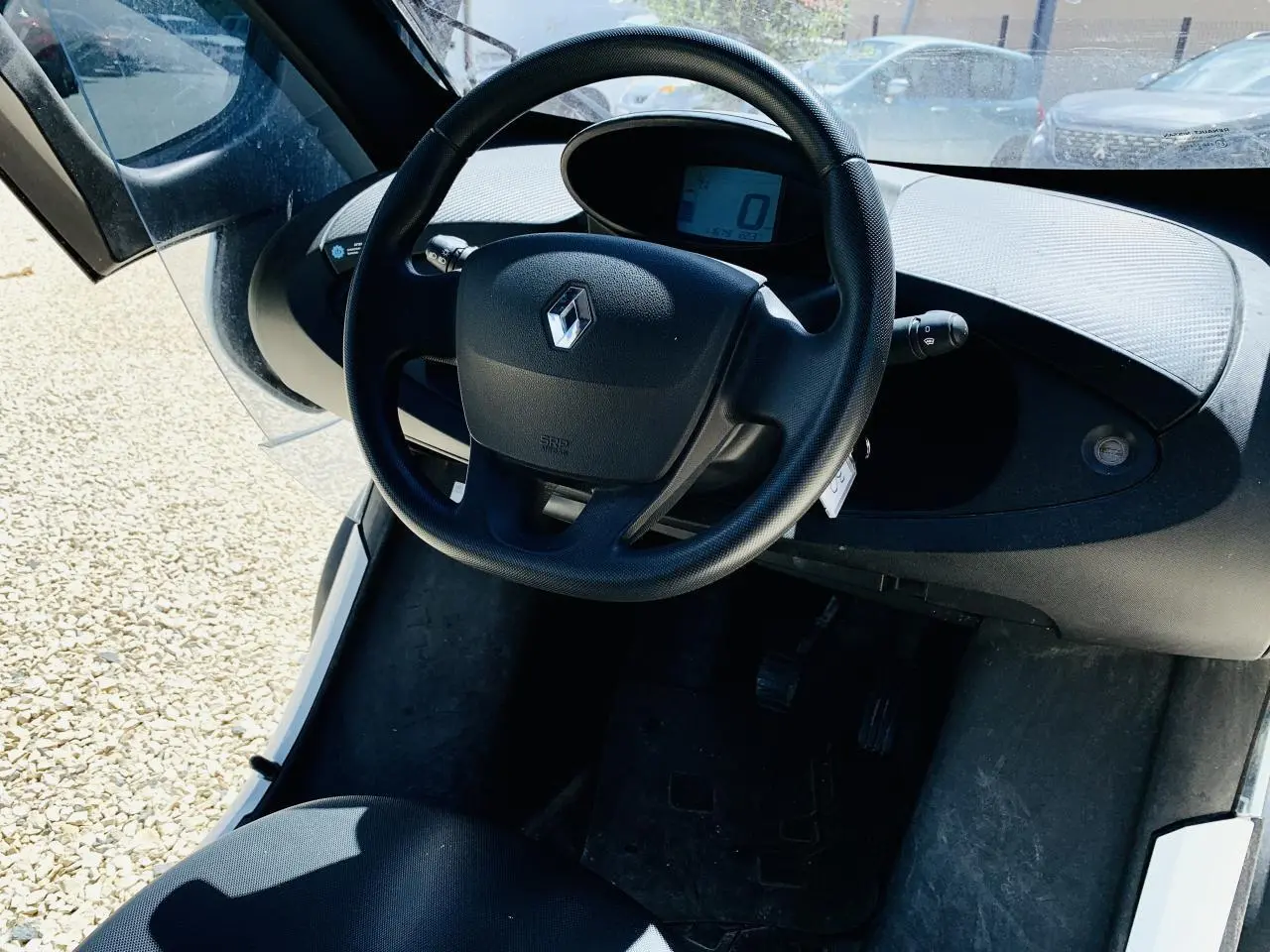 Vue intérieure centrée sur le volant noir et le tableau de bord digital d'une Renault Twizy blanche 2019.