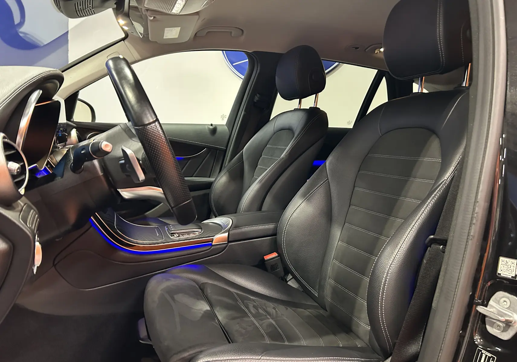 Vue intérieure côté conducteur du Mercedes GLC 220D AMG Line 2021 avec sièges cuir noir et éclairage d'ambiance bleu.