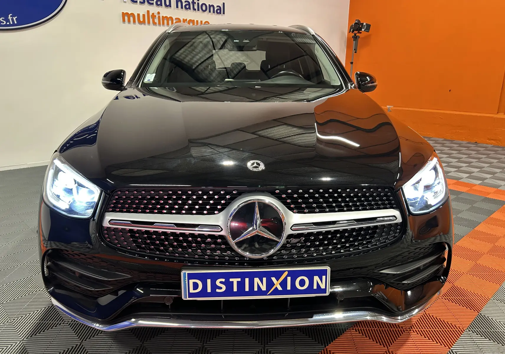 Vue frontale d'un Mercedes GLC 220D AMG Line noir Obsidienne métallisé avec phares allumés et calandre distinctive AMG.