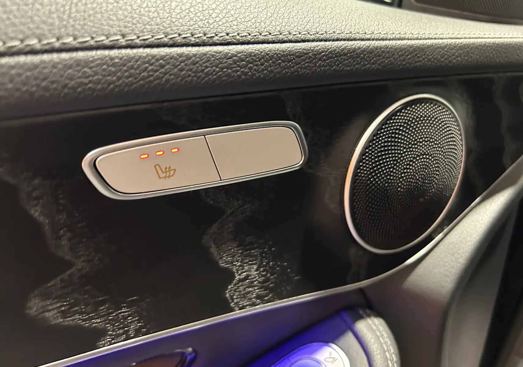Détail intérieur côté gauche avec commande de siège chauffant active et haut-parleur rond sur panneau noir brillant.