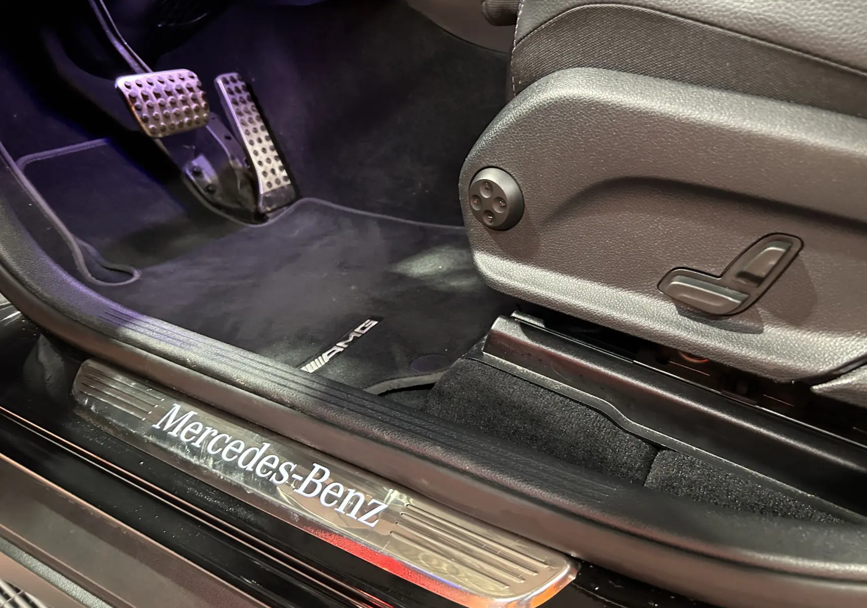 Gros plan intérieur côté conducteur du Mercedes GLC 220D AMG Line noir, avec seuil de porte Mercedes-Benz et tapis AMG.