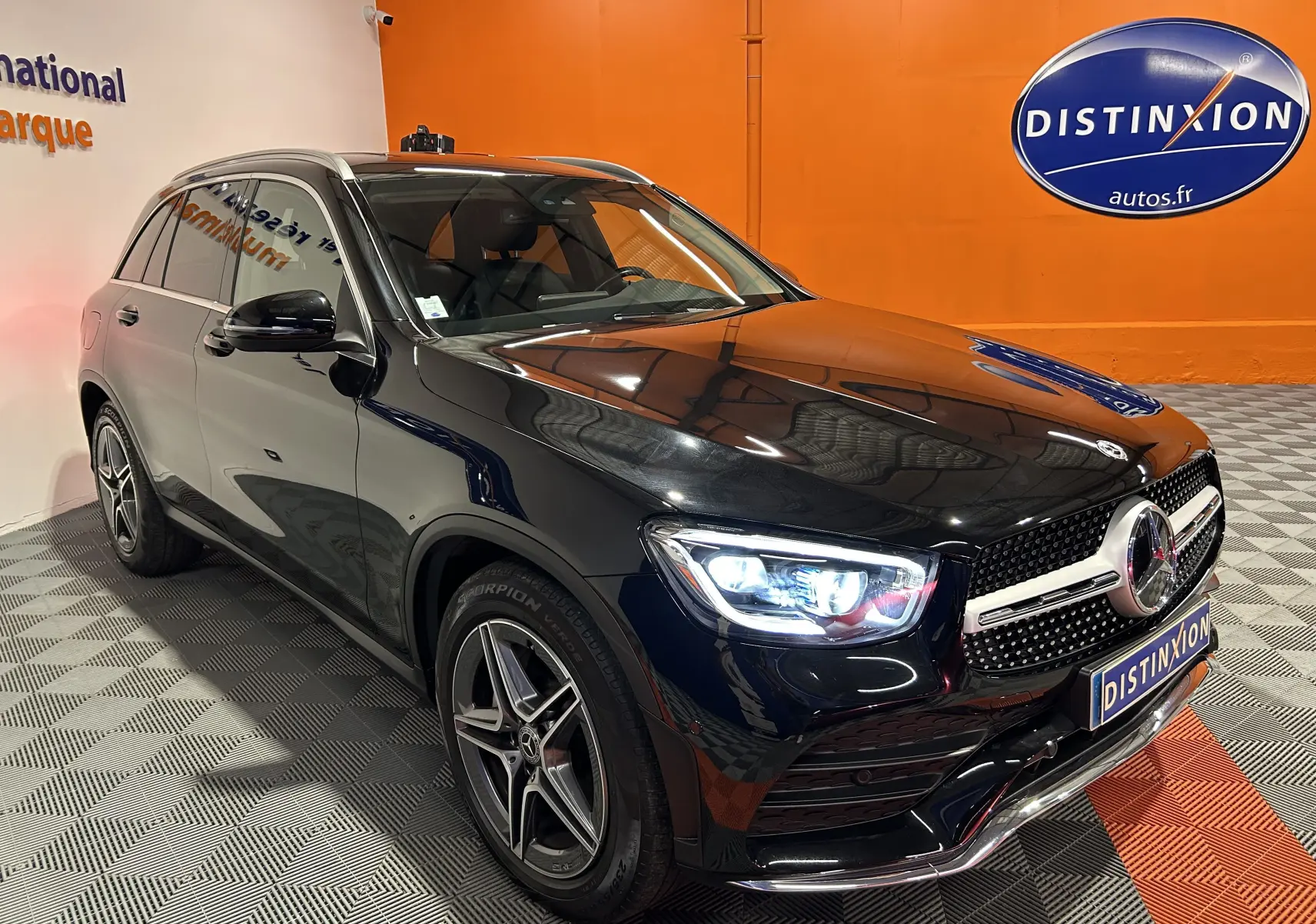 Mercedes GLC 220D AMG Line noir Obsidienne métallisé, vue 3/4 avant droit avec phares allumés en intérieur showroom.