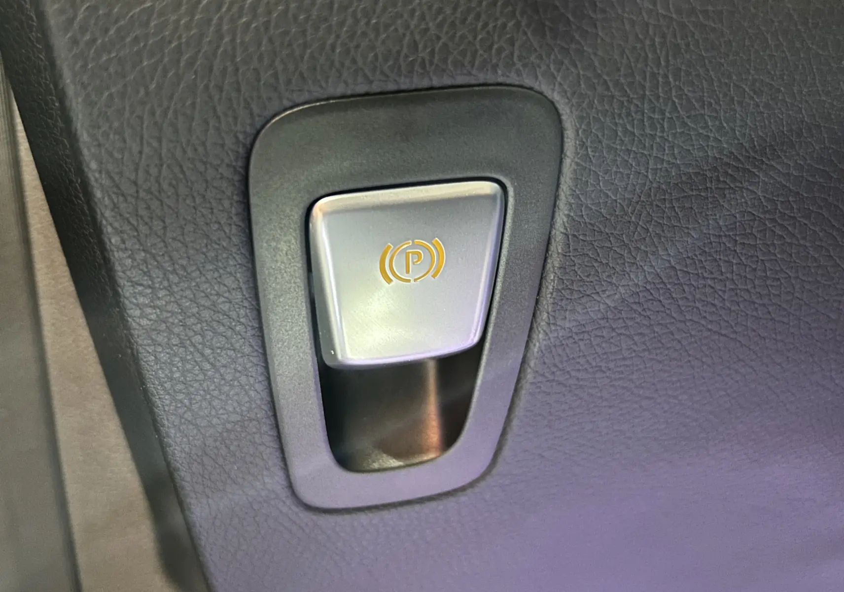 Bouton de frein à main électronique argenté sur fond de cuir noir à l'intérieur d'une Mercedes GLC 220D AMG Line 2021.