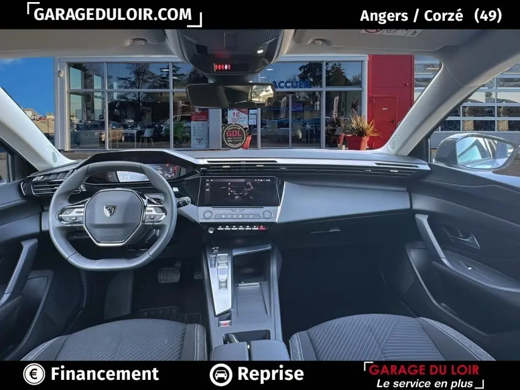 Vue intérieure avant de la Peugeot 308 2023 gris clair, tableau de bord moderne avec écran tactile central et volant cuir multifonctions.