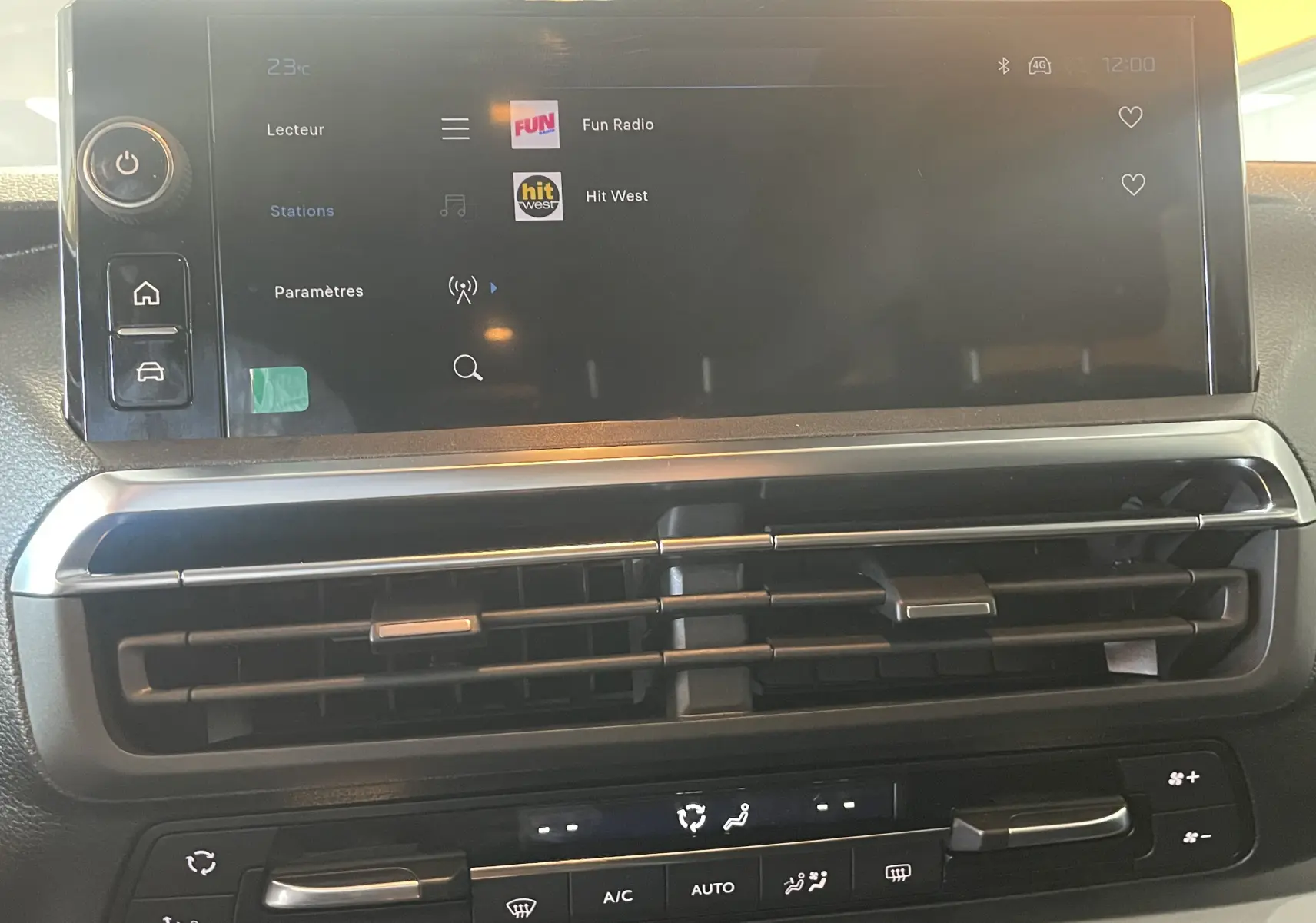 Vue rapprochée de l'écran tactile et des commandes de climatisation du Peugeot Traveller noir, avec affichage radio et ventilation centrale.