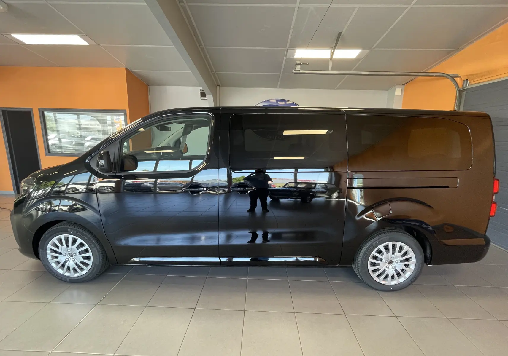 Profil côté gauche du Peugeot Traveller noir 2026 en intérieur, avec portes coulissantes et jantes alliage visibles.