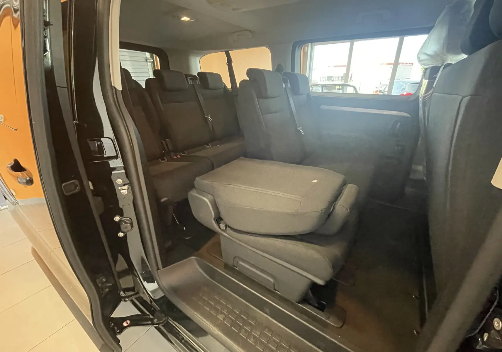 Vue intérieure côté droit du Peugeot Traveller noir 2026, montrant les sièges arrière et une banquette rabattue.