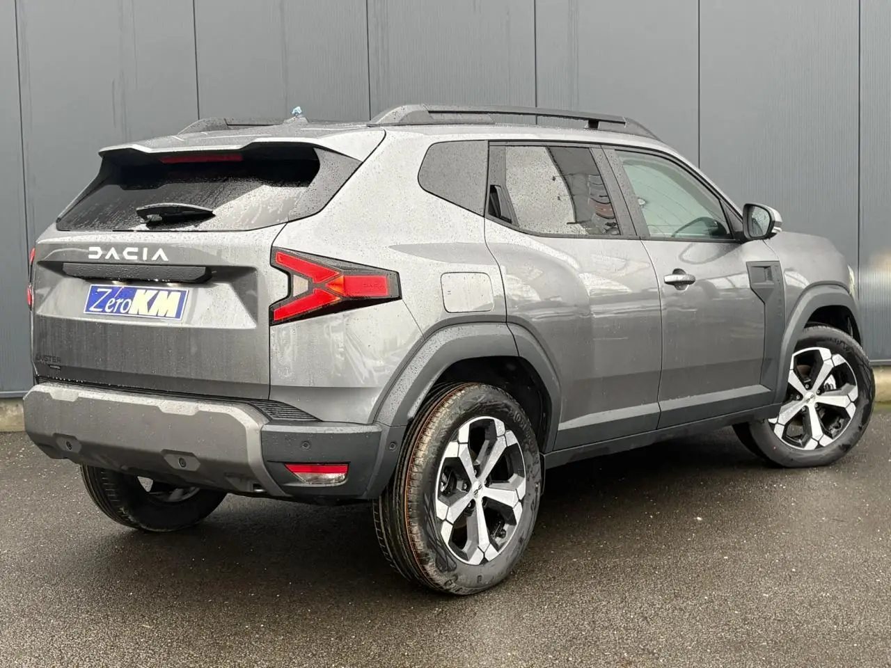 Vue 3/4 arrière droite du Dacia Duster gris schiste avec jantes alliage diamantées et barres de toit noires.