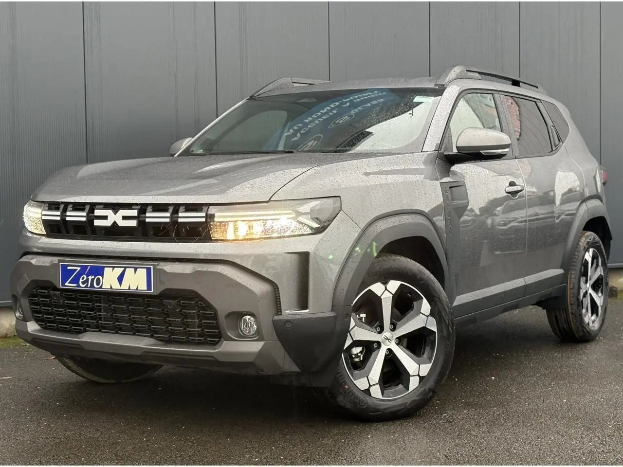SUV Dacia Duster gris schiste en 3/4 avant droit, avec jantes alliage diamantées et signature lumineuse LED allumée.
