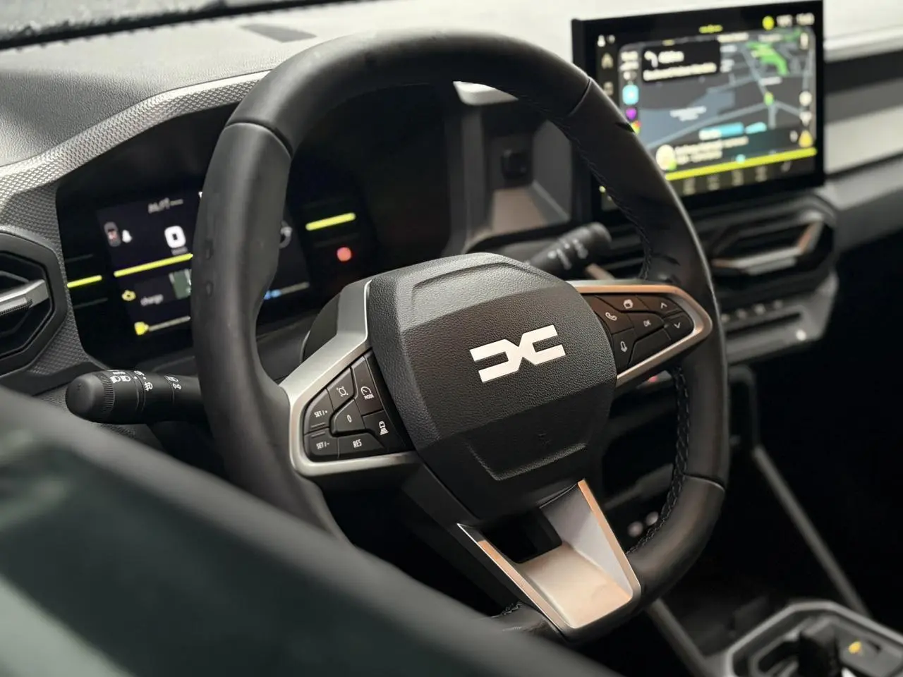 Vue rapprochée du volant noir au logo DACIA stylisé, avec tableau de bord digital et écran tactile central du Dacia Duster 2026.