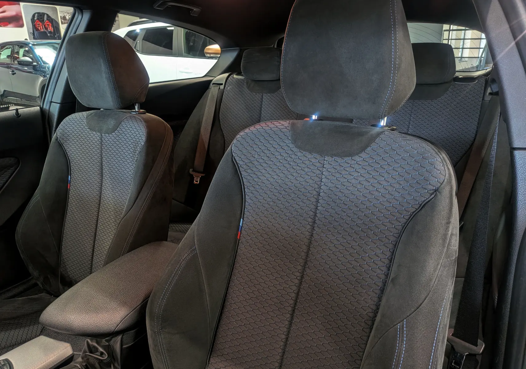 Intérieur de BMW Série 1 F21 118d M Sport 2014, vue rapprochée des sièges avant en tissu noir avec surpiqûres bleues.