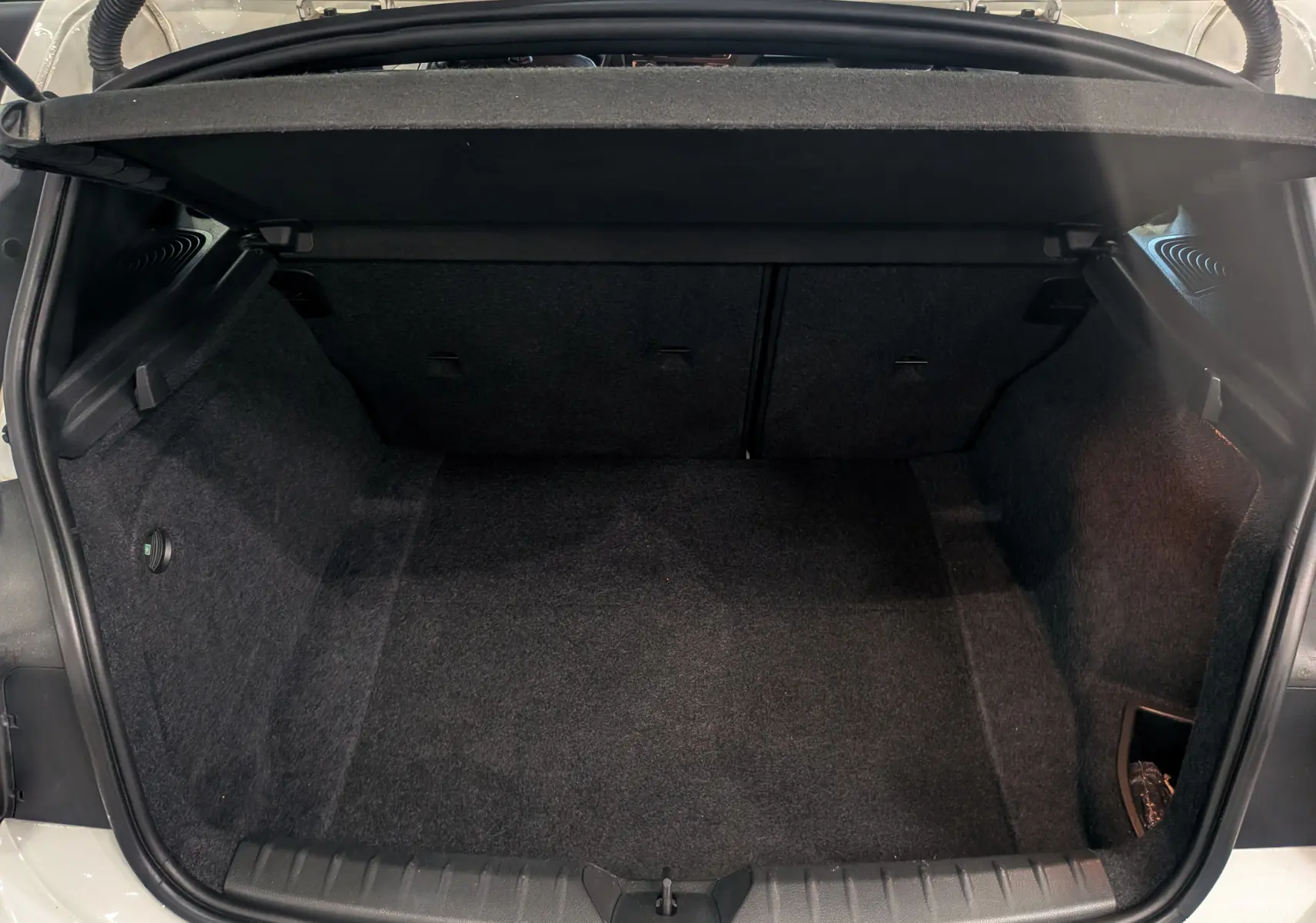 Coffre ouvert vu de l'arrière d'une BMW Série 1 F21 blanc alpin, montrant un espace de chargement propre et vide.