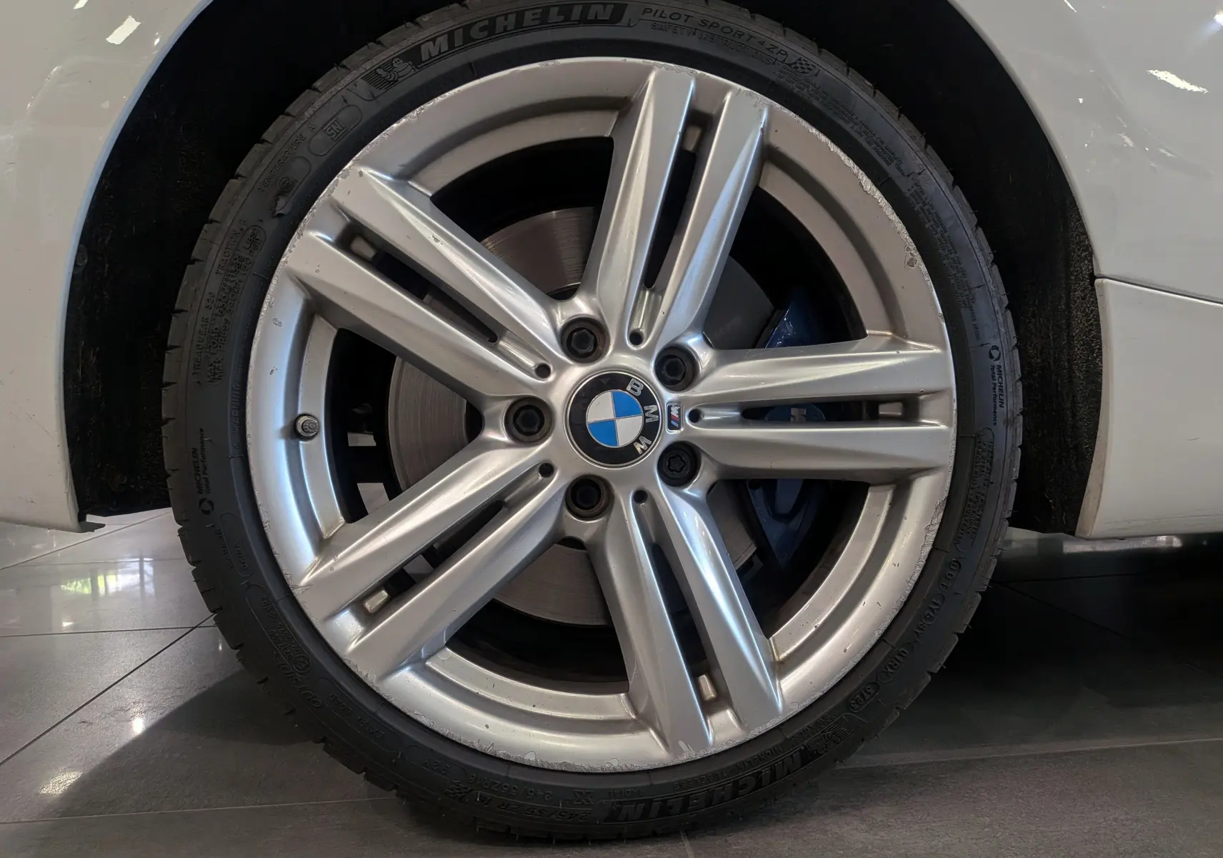 Gros plan sur la jante alliage argentée et le pneu Michelin d'une BMW Série 1 F21 blanc alpin.