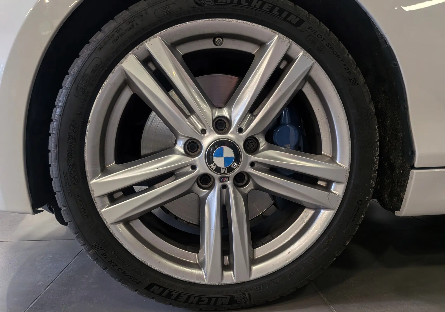 Gros plan sur la jante alliage 18 pouces et le frein bleu d'une BMW Série 1 F21 blanche Alpine côté avant droit.