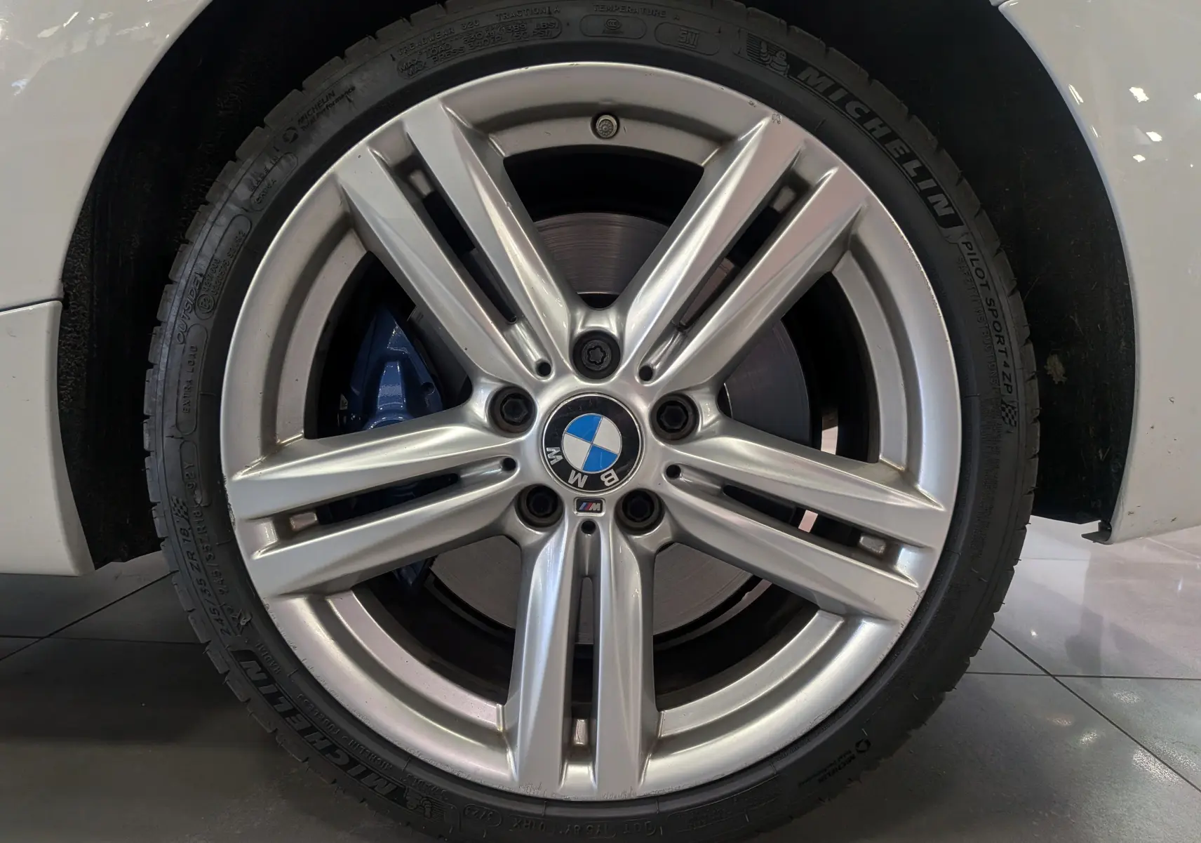 Gros plan sur la jante alliage argentée avec logo BMW et étrier de frein bleu sur roue avant droite d'une BMW Série 1 blanche.