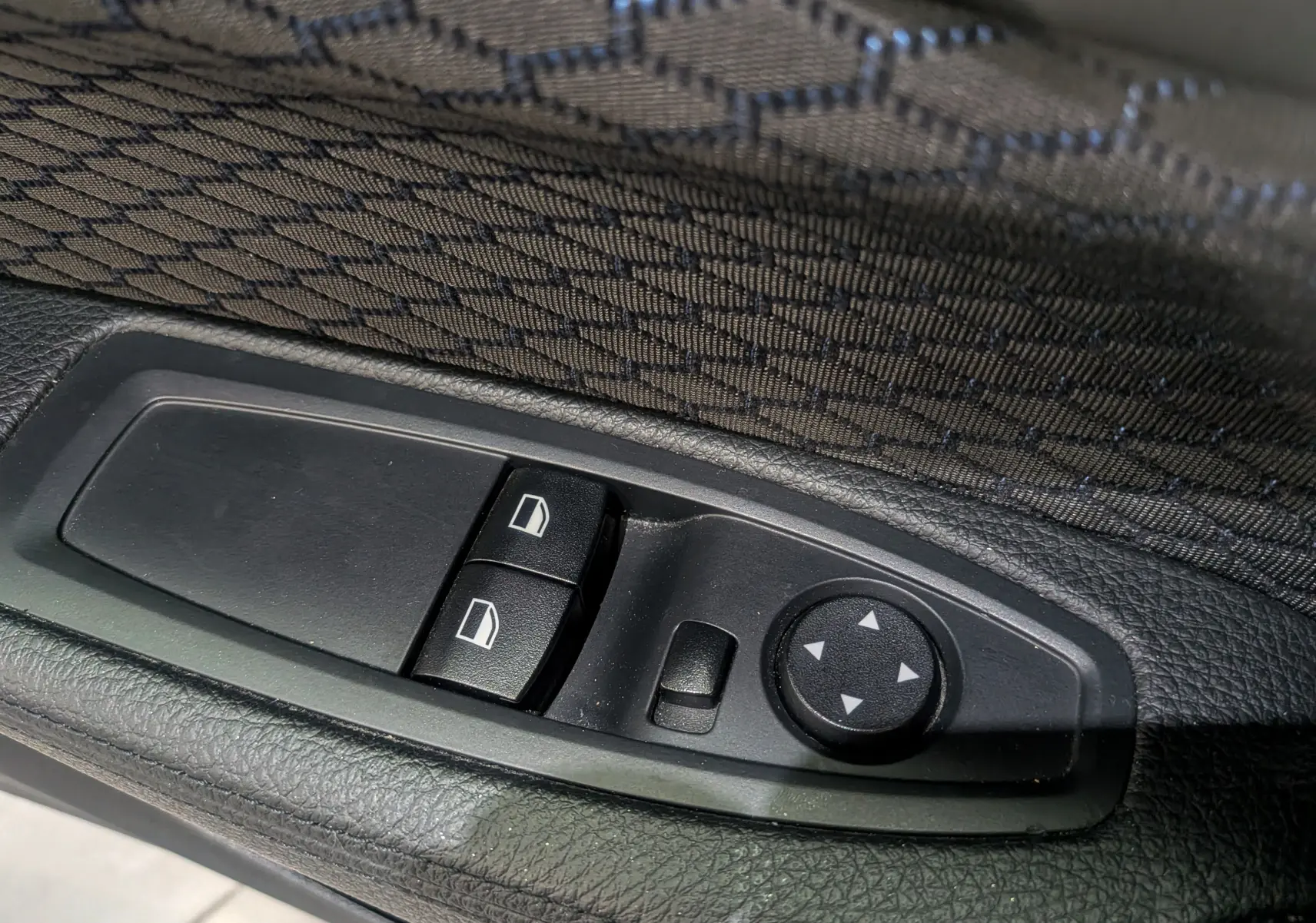 Gros plan sur les commandes de lève-vitres et réglage des rétroviseurs côté conducteur d'une BMW Série 1 F21 blanche.