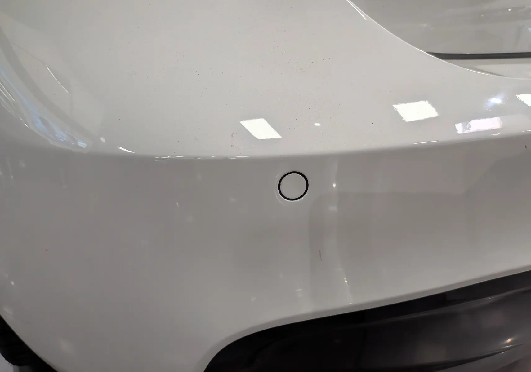 Gros plan sur le pare-chocs arrière blanc alpin d'une BMW Série 1 F21 118d xDrive M Sport avec capteur de recul visible.
