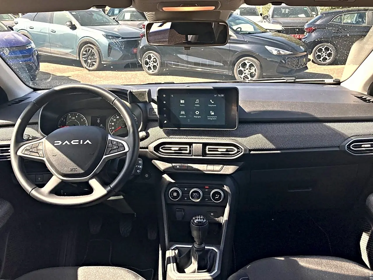 Vue intérieure avant de la Dacia Sandero 2025, tableau de bord noir avec écran tactile et volant multifonctions.