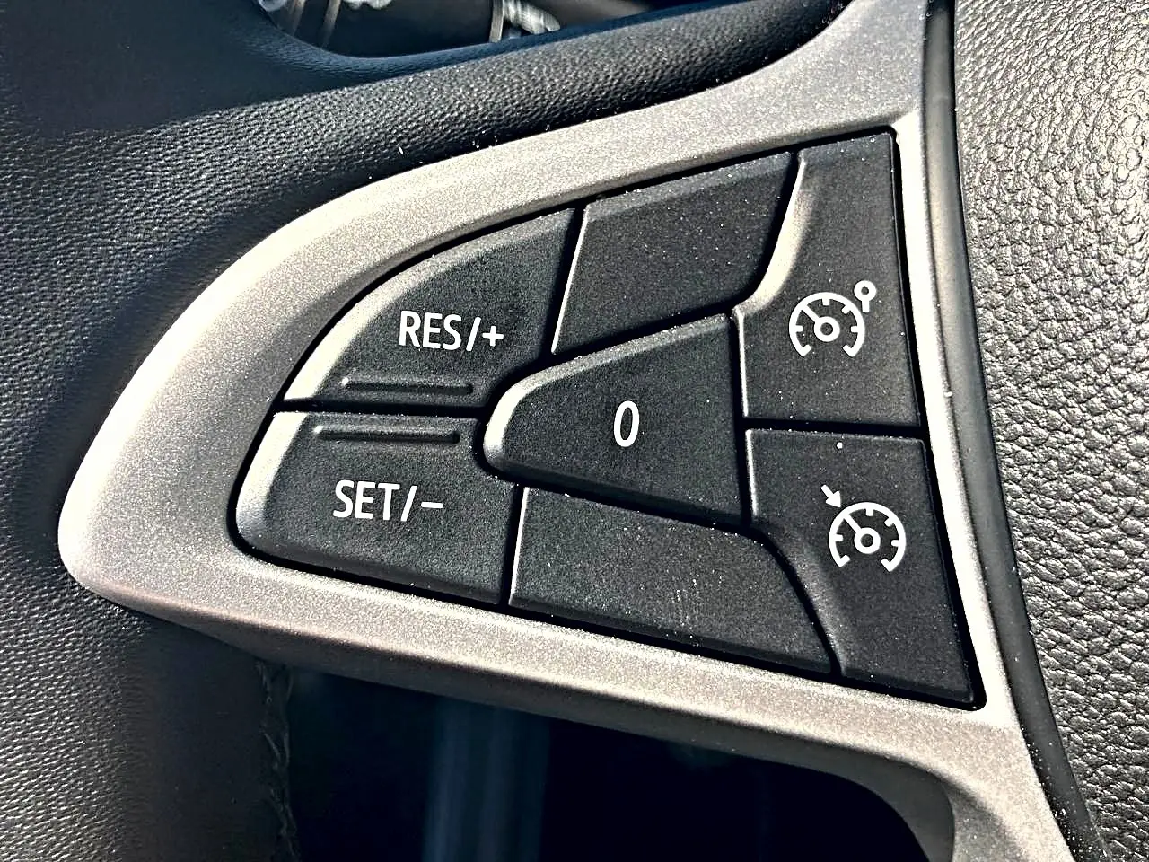 Gros plan sur les commandes noires du régulateur de vitesse sur le volant de la Dacia Sandero blanche.