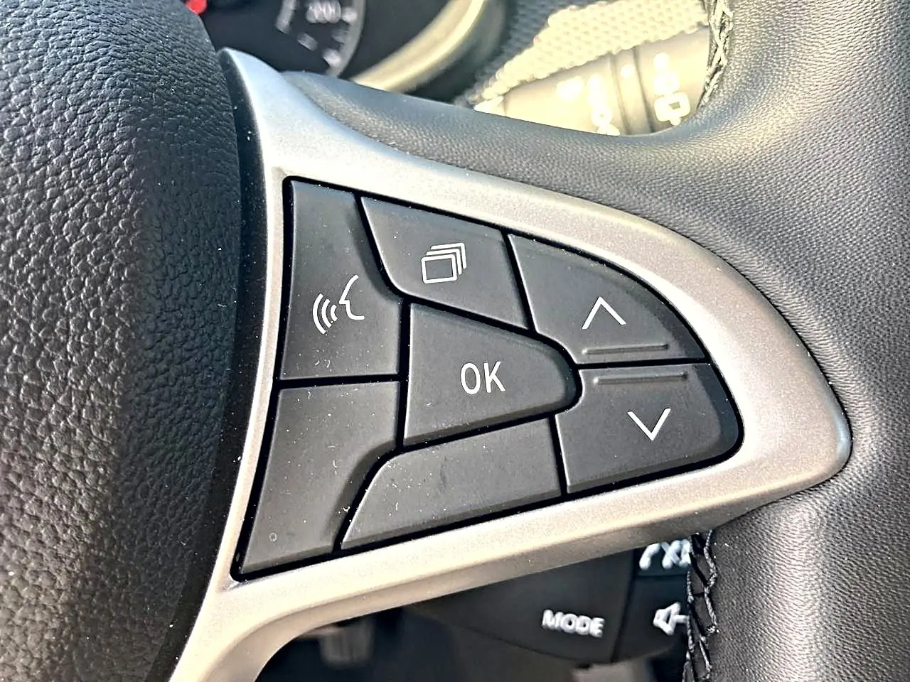 Gros plan sur les commandes noires du volant de la Dacia Sandero blanche, avec boutons multifonctions et finition argentée.