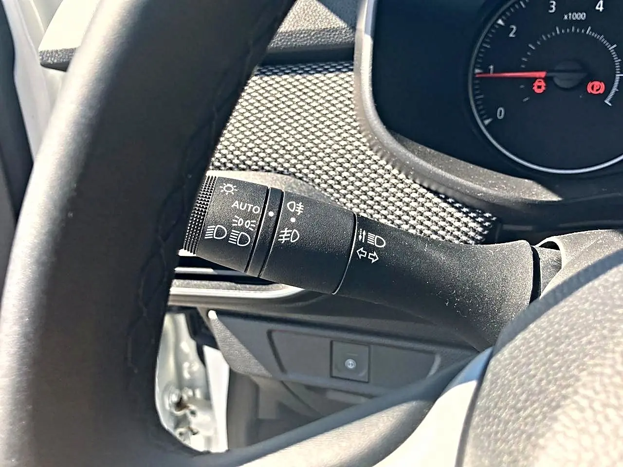 Gros plan sur la commande des phares et clignotants côté gauche du tableau de bord d’une Dacia Sandero blanche 2025.