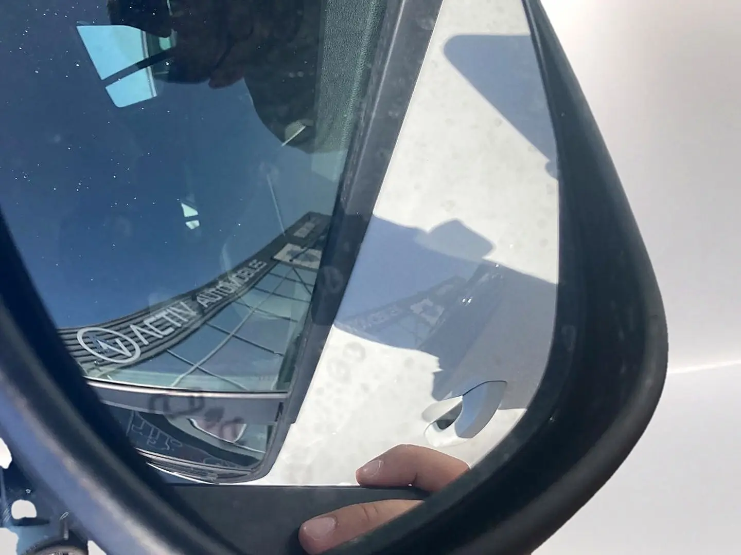 Rétroviseur côté droit d’une Dacia Sandero blanche 2025, avec reflet partiel de la carrosserie et main visible.
