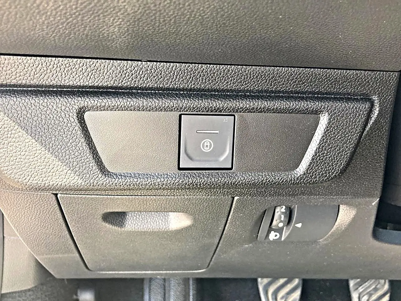Gros plan sur le bouton de verrouillage centralisé noir dans l'habitacle de la Dacia Sandero blanche, côté conducteur.